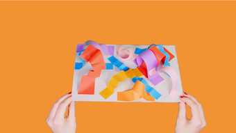 hands against an orange background holding a paper sculpture