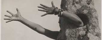 sepia phtograph of arms reaching out of a rock like suit 