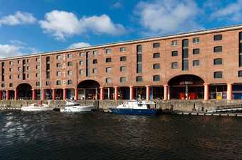 tate liverpool on the albert dock as seen from across the water. there are boats in the water and the sky is blue.
