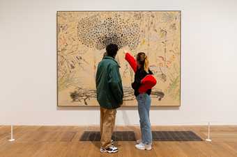 two visitors stand and look at a painting, there is a barrier around it