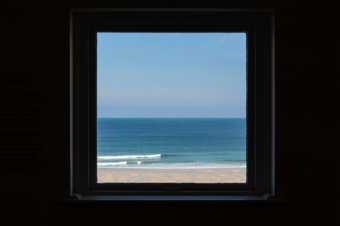 view of a blue sky, sea and sandy beach seen through a square window