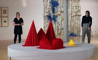 A photograph of two visitors looking at a bright red and yellow sculpture by Anish Kapoor