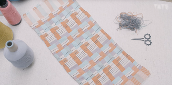 photograph of a pastel weaved piece of material with reels of threads and scissors