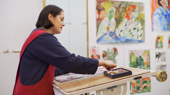 Photograph of a woman drawing with pastels and standing at an easel